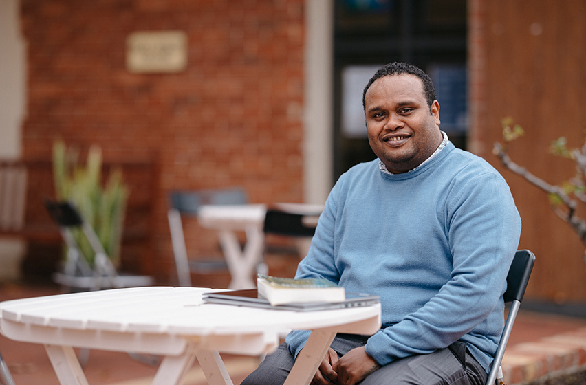 Postgraduate arts and sciences male student wearing a blue jumper sitting at the courtyard of Fremantle campus 