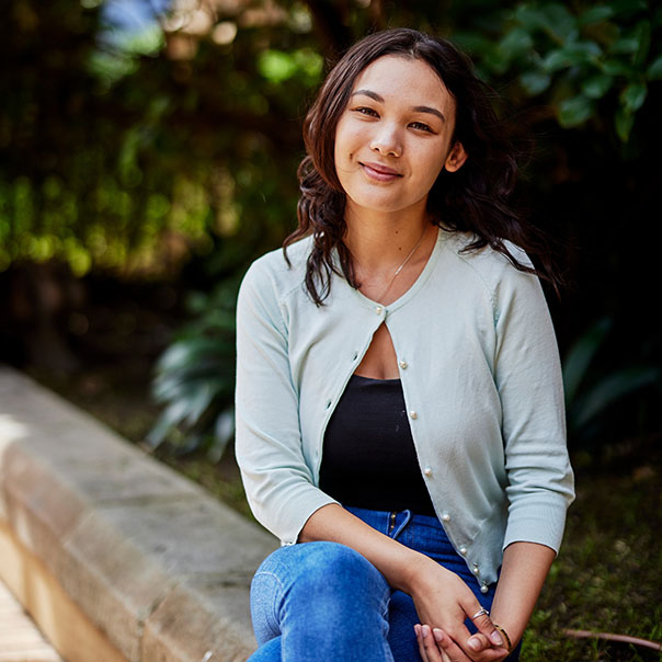 Postgraduate Notre Dame female student wearing a grey cardigan sitting outside at the Sydney campus 